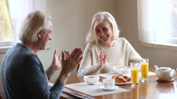 Счастливая пожилая пара разговаривает смеясь, имея здоровый завтрак утром — стоковое видео