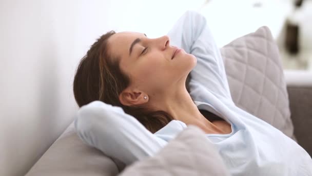 Спокойная расслабленная молодая женщина отдыхает опираясь на удобный мягкий диван — стоковое видео