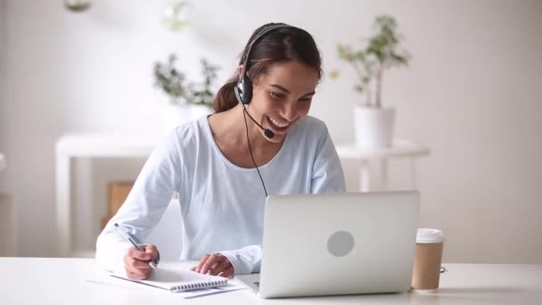 Mujer feliz en auriculares hablando por webcam haciendo notas — Vídeo de stock