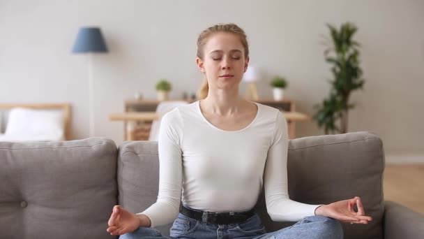 Ruhige, gelassene Frau, die zu Hause auf der Couch sitzt und meditiert — Stockvideo