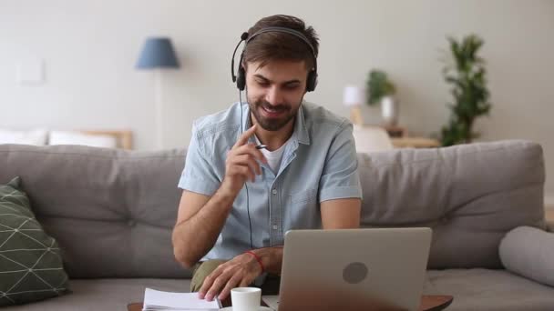 Счастливый человек в гарнитуре, говорящий по веб-камере, глядя на ноутбук — стоковое видео
