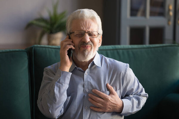 Седой мужчина трогает грудь, у него сердечный приступ, он вызывает скорую.
