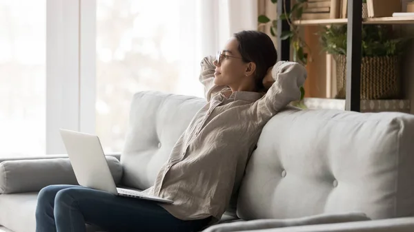 Mujer serena con computadora en vueltas apoyada en el sofá descansando — Foto de Stock