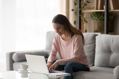 Evde kanepede oturan freelancer kadın bilgisayar başında çalışıyor