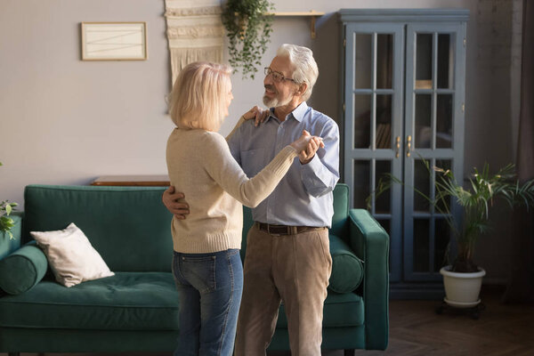 Happy mature loving couple, wife and husband dancing at home