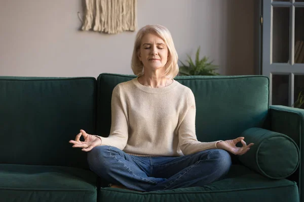 Mulher madura de cabelos grisalhos meditando, praticando ioga em casa — Fotografia de Stock