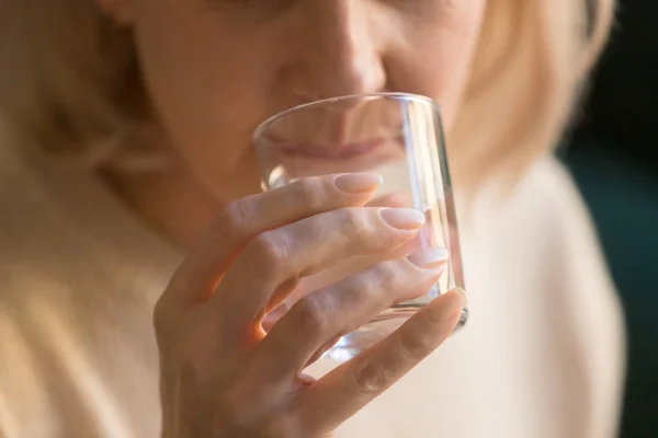 Закройте зрелую женщину, пьющую чистую воду, держа в руке стекло — стоковое фото