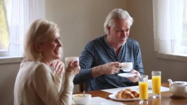 Neşeli yaşlı eşler masada oturup sabah kahvesi içerken konuşuyorlar.