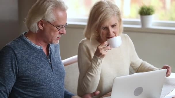 Веселая пожилая жена пьет кофе в чате с мужем с помощью ноутбука — стоковое видео