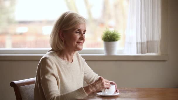 Пожилая женщина пьет кофе, забытый приятными мыслями и воспоминаниями — стоковое видео