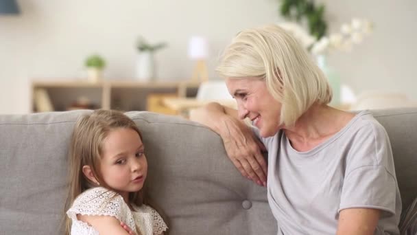 Niedliche kleine Enkelin im Gespräch mit Oma, die Spaß auf dem Sofa hat — Stockvideo