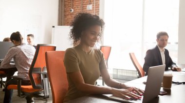 Paylaşılan ofiste dizüstü bilgisayar üzerinde çalışan gülümseyen siyah kadın çalışan