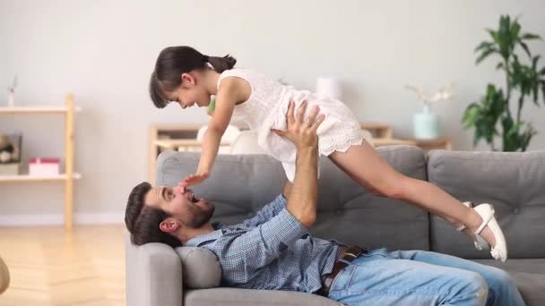 Happy father lying on couch lifting child daughter having fun — Stock Video
