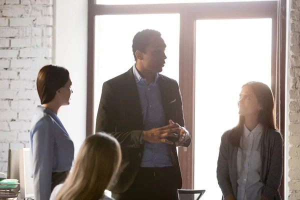 Black boss giving instructions to employees during briefing at office