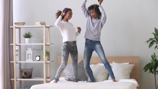 Счастливые черные мама и дочь в наушниках танцуют на кровати — стоковое видео