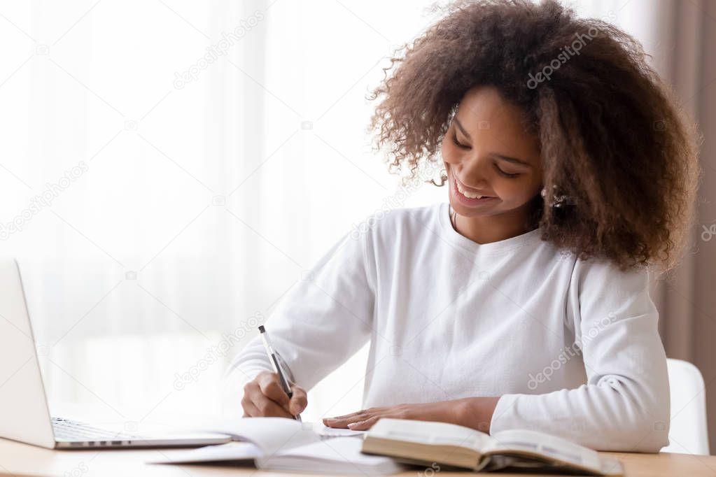 Smiling African American teen girl preparing school homework, using laptop