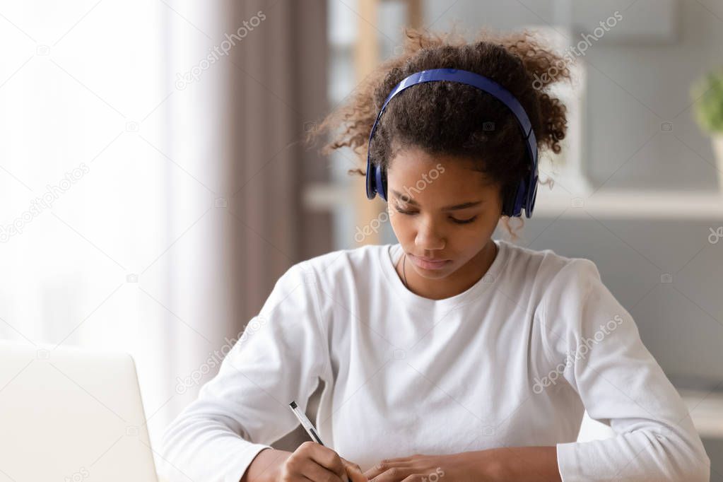 African American teenage girl wearing headphones, doing homework