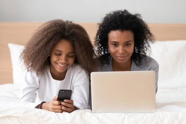 Afro-Amerikan anne ve kızı birlikte dizüstü bilgisayar ve telefon kullanarak — Stok fotoğraf