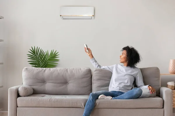 Glimlachend Afro-Amerikaanse vrouw met behulp van Air Conditioner afstandsbediening — Stockfoto