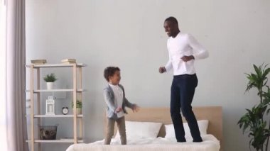 Mutlu kaygısız Afrikalı baba ve çocuk oğlu yatakta atlama