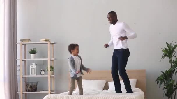 Gelukkig zorgeloos Afrikaanse vader en Kid zoon springen op bed — Stockvideo