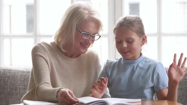 Gamla farmor hjälpa barnbarn skolan barnflicka med läxor — Stockvideo