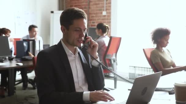 İş masasında dizüstü bilgisayar kullanarak telefonda konuşan erkek işçi — Stok video