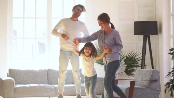 Счастливые родители и дочь смеются, танцуя в гостиной — стоковое видео