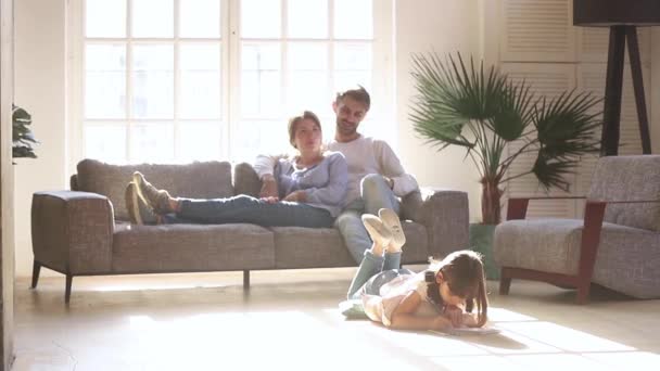 Parents se détendre sur le canapé tandis que la fille enfant dessin sur le sol — Video