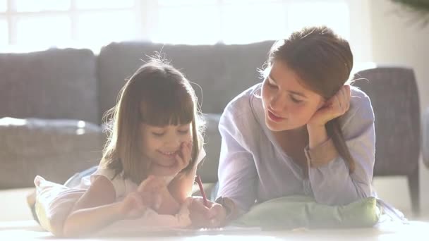 Заботливая мама раскрашивает рисунок карандашами разговаривая с девочкой — стоковое видео