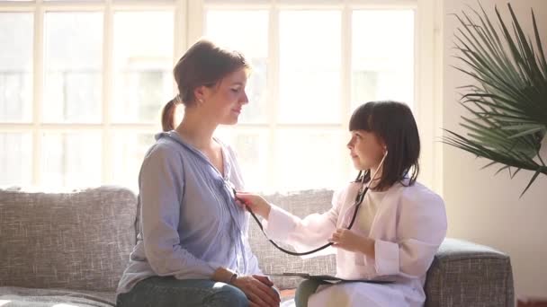 Дівчинка одягнена в уніформу, як лікар грає з мамою — стокове відео