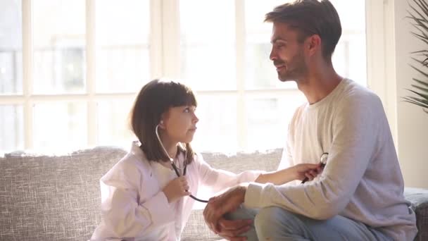 Lindo niño hija sosteniendo estetoscopio escuchando padre paciente — Vídeos de Stock