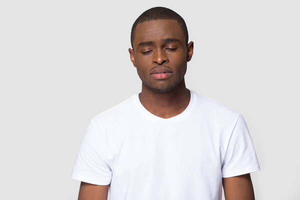 Head shot studio portrait over grey blank isolated dark-skinned sad man wearing white t-shirt feels frustrated and unhappy having broken heart personal problems, desperate guy misunderstanding concept