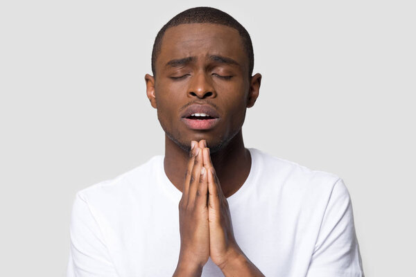 African millennial man closed eyes cupped hands and praying