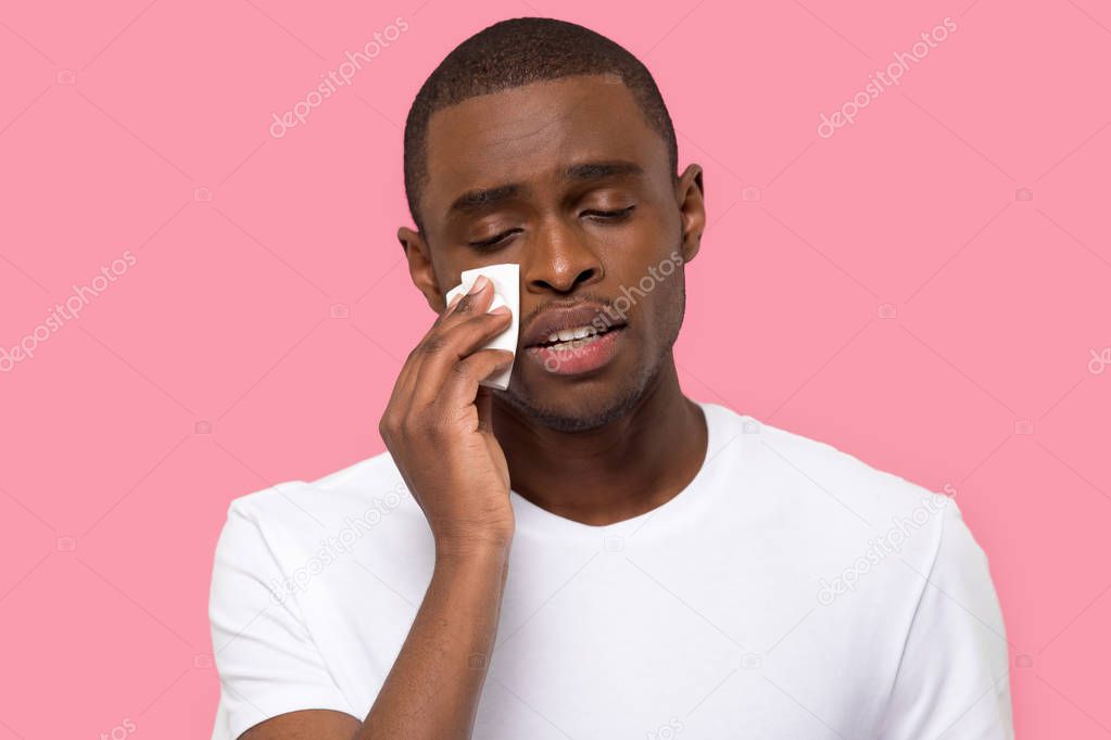 African male wiping tears feels unhappy posing over pink background