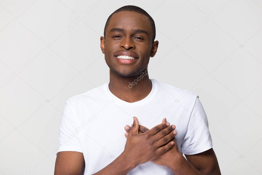 Headshot portrait african male holding hand on heart feels gratitude