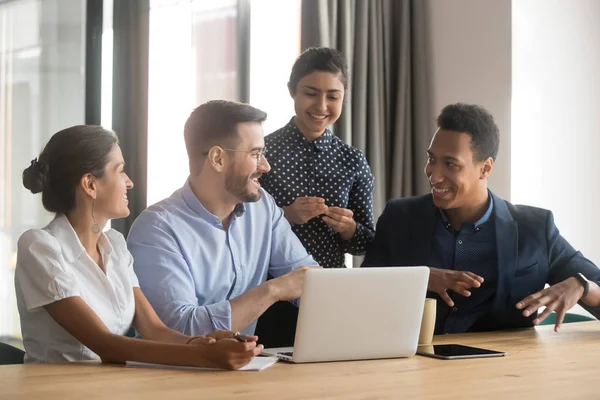 Sonriendo diversos empleados hablan de lluvia de ideas en la oficina utilizando el ordenador portátil — Foto de Stock