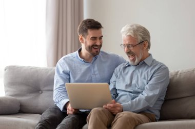Gülümseyen yetişkin oğlu ve üst düzey baba birlikte dizüstü bilgisayar kullanarak gülmek