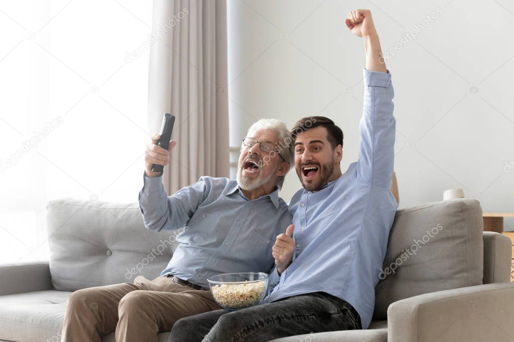 Excited elderly dad and son cheering watching TV game together