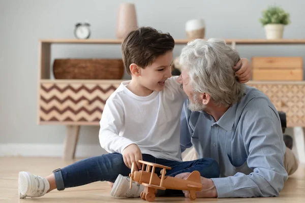 Улыбающийся дедушка играет с маленьким внуком дома — стоковое фото