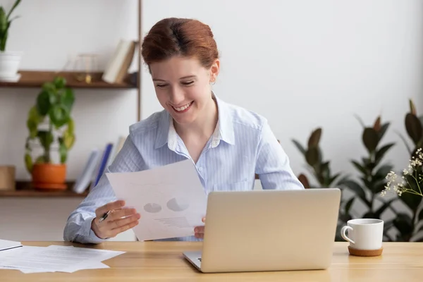 Удовлетворенная улыбающаяся женщина сидит за столом и работает с деловыми документами — стоковое фото