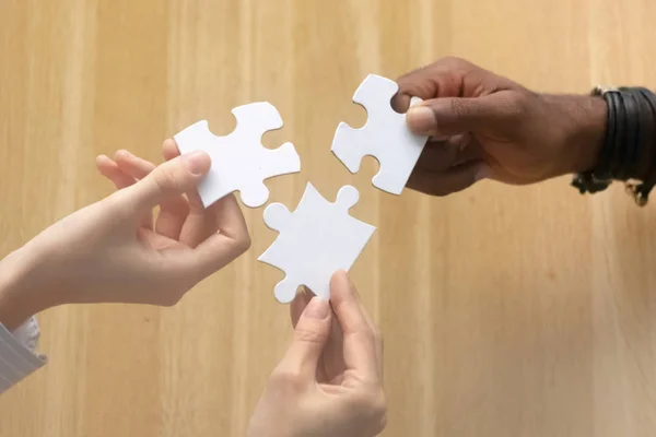 Multiracial female male hands holding puzzle pieces above table — Stock Photo, Image