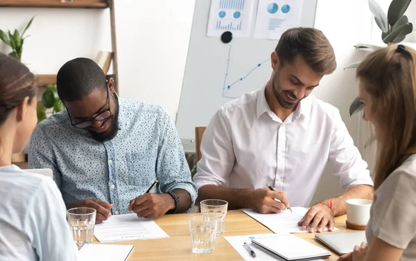 Счастливые улыбающиеся бизнесмены ставят подпись на бумажном документе — стоковое фото