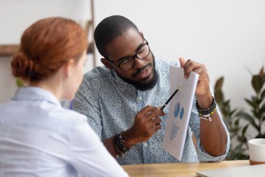Kadın iş arkadaşına proje sonuçlarıyla belge gösteren erkek iş arkadaşı
