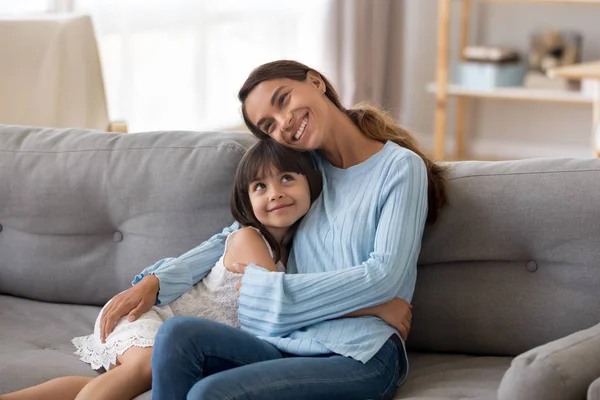 Jolie fille heureuse câlin jeune maman assise sur le canapé — Photo