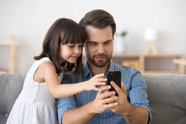 スマートな小さな女の子と若いお父さんは、スマートフォン上で画像を作ります — ストック写真