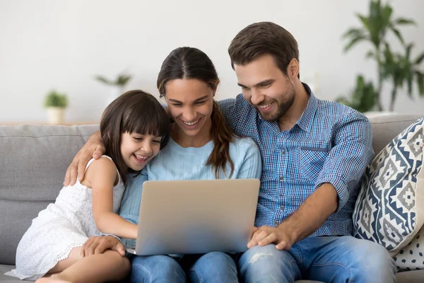 Smiling parents with kid watch funny movie on laptop