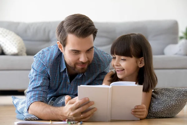 Cuidar do pai deitado no chão gosta de ler com a pequena filha — Fotografia de Stock