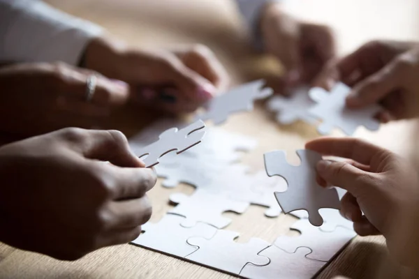 Close up members of multiracial team assembling white puzzle — Stock Photo, Image