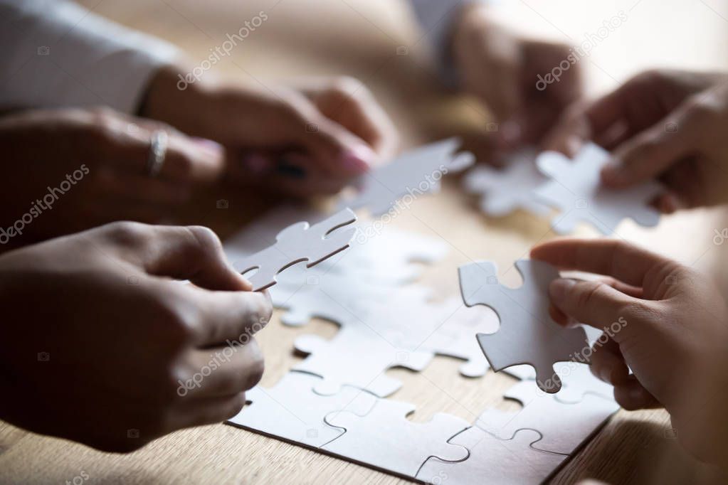 Close up members of multiracial team assembling white puzzle